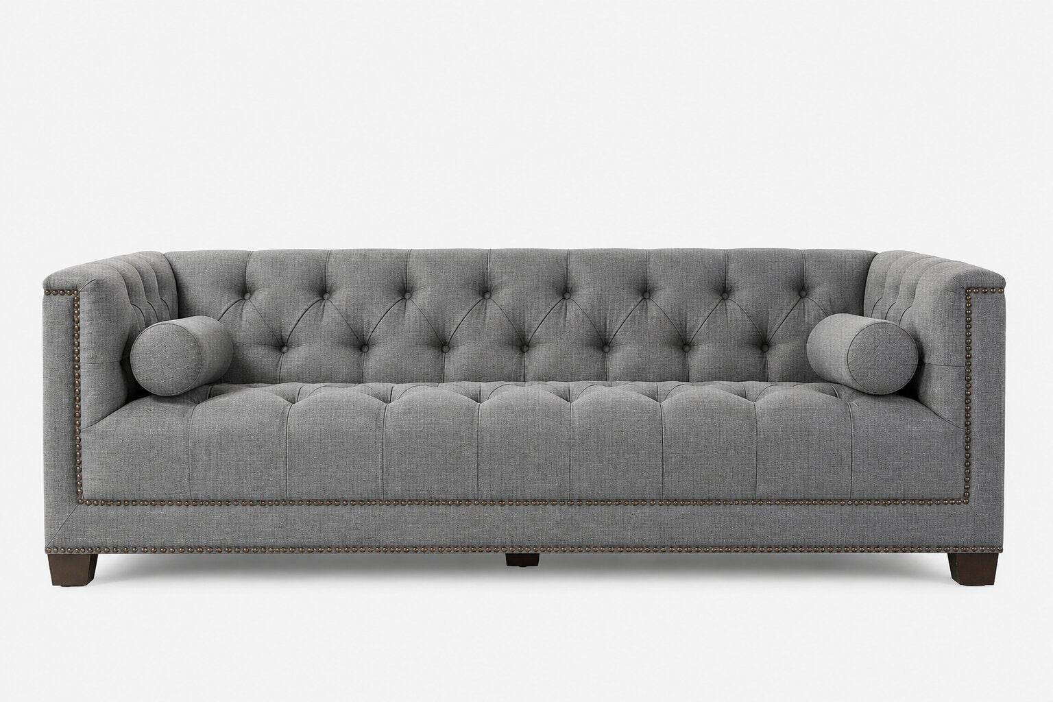 A gray tufted fabric sofa with cylindrical bolsters, nailhead trim, and dark wooden legs, shown against a plain white background.