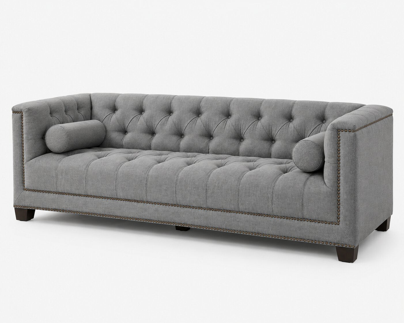 A gray tufted Chesterfield-style sofa with cylindrical bolsters, nailhead trim, and dark wooden legs, shown on a plain light gray background.