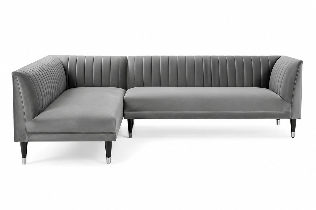A modern gray velvet sectional sofa with vertical channel tufting on the backrest and arms, supported by slim black legs with silver tips, shown against a plain white background.