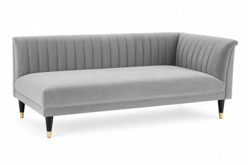 A modern gray velvet corner sofa with vertical channel tufting on the backrest and arms, supported by black tapered legs with gold caps, shown on a white background.