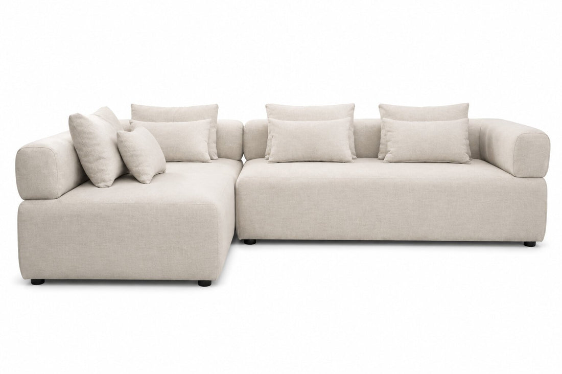 A modern modular sectional sofa upholstered in a light beige textured fabric, featuring a left-facing chaise lounge section and multiple matching throw pillows, shown against a plain white background.