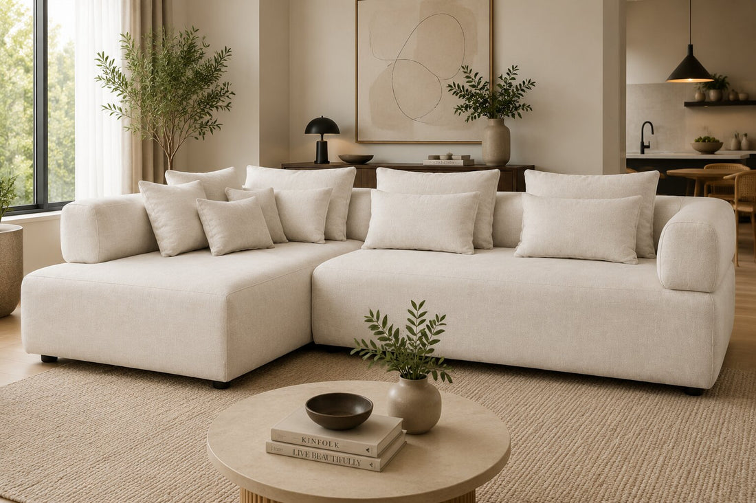 A modern modular sectional sofa upholstered in a light beige textured fabric, featuring a left-facing chaise lounge section and multiple matching throw pillows, shown against a plain white background.