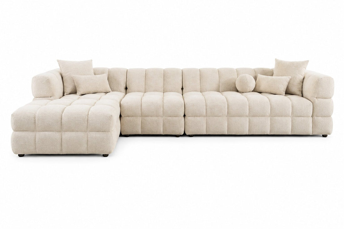 A modern sectional sofa in a light beige tufted fabric, featuring a left-facing chaise lounge and multiple matching throw pillows, shown against a plain white background.