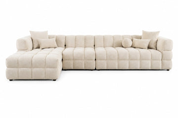 A modern sectional sofa in a light beige tufted fabric, featuring a left-facing chaise lounge and multiple matching throw pillows, shown against a plain white background.