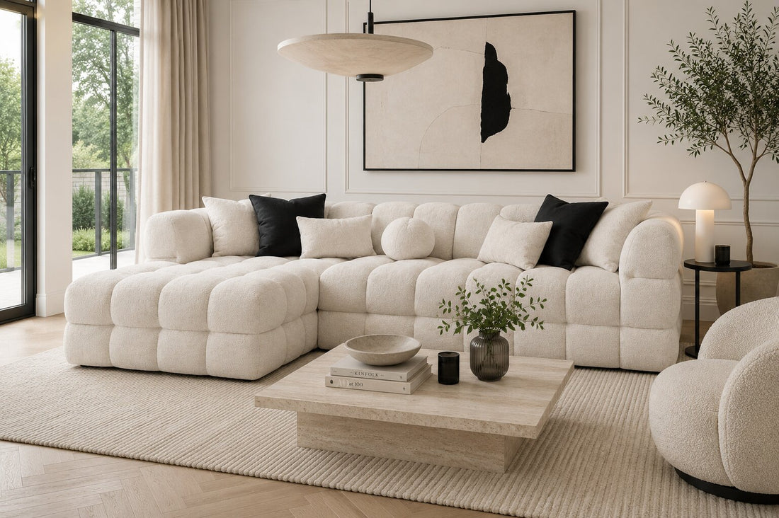A modern modular sectional sofa in a light beige tufted fabric, styled with black accent pillows and a matching round throw pillow, set against a plain white background.