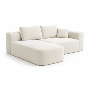 A modern modular sectional sofa upholstered in a light cream fabric, featuring a low-profile chaise lounge on the left, two back cushions, and a right armrest, shown on a solid white background.