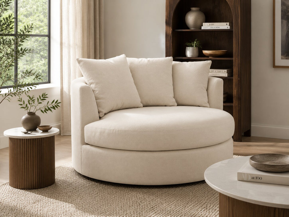 A round upholstered lounge chair in a light beige fabric with three matching back cushions, shown on a plain white background.